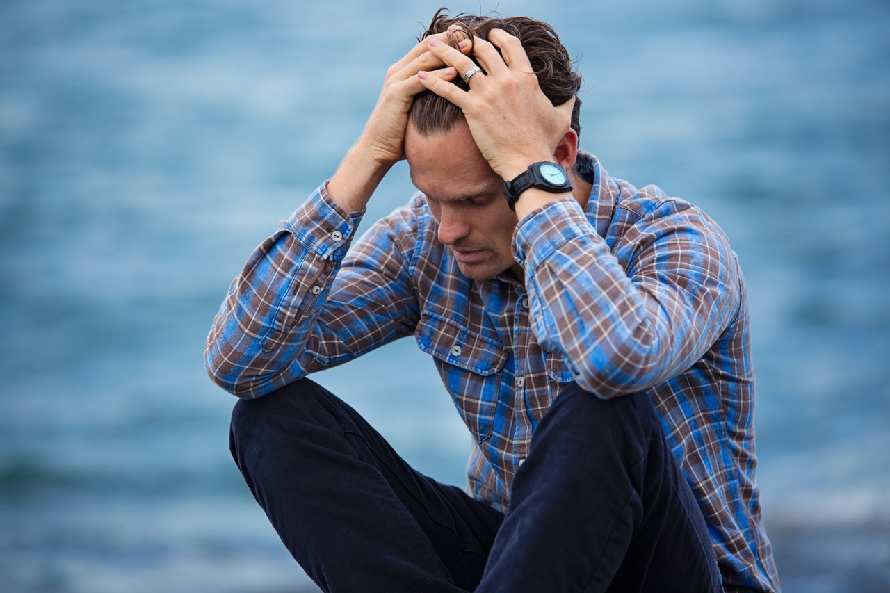 Man with fingers through hair seeming depressed, anxious, worried.